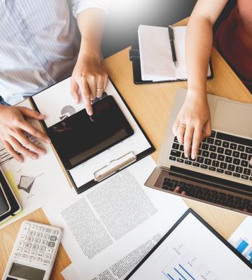 Professionals working at a table with lots of documents, a laptop and tablet.