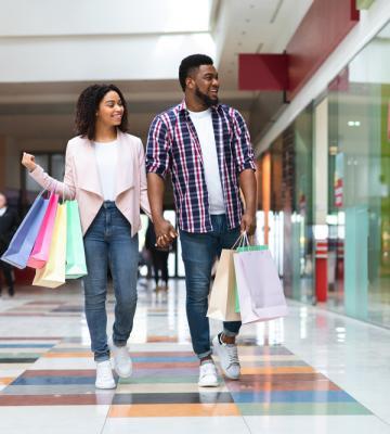 A couple holding hands and holding many shopping bags while walking.