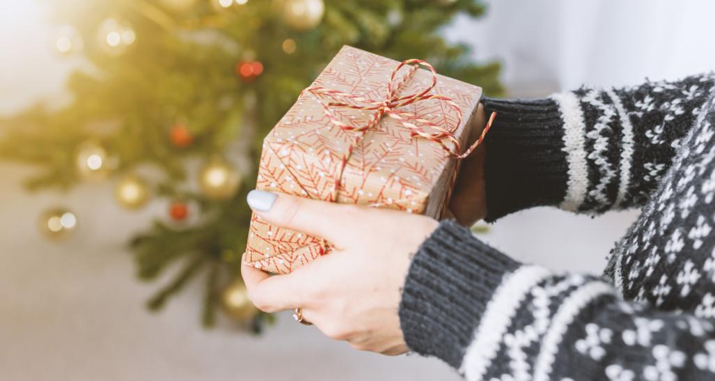 a lady is holding a christmas present in front of a christmas tree during the holiday season