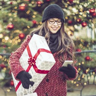 Young woman holds wrapped gift and looks at phone while holiday shopping